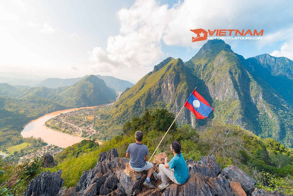 motorbike tours laos-couple-conquering-mountain-top-nong-khiaw-panoramic-view-nam-ou-river-valley-laos-national-flag-scenic-mountain-landscape-1